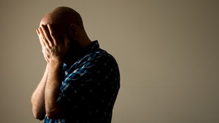 Ein Mann verbirgt sein Gesicht, weil er einsam ist. So geht es vielen Menschen in Deutschland. 