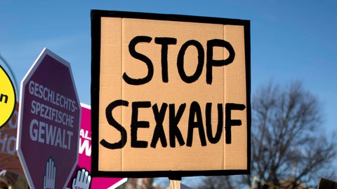 Bei einer Demo wird ein Schild mit der Aufschrift "Stop Sexkauf" hochgehalten.