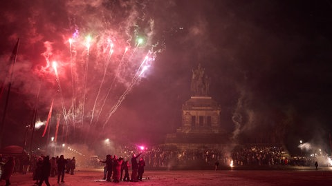 Menschen feiern vor der Reiterstatue am Deutschen Eck in Koblenz Silvester.