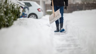 Ein Mann schippt und räumt Schnee weg - wer in RLP der Räumpflicht nicht nachkommt, dem droht ein Bußgeld.