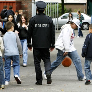 Ein Polizist zwischen Schülerinnen und Schülern auf einem Schulhof - Mehr Präsenz soll die Sicherheit stärken (Archivbild)