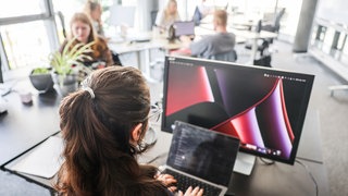 Auch in RLP tobt eine Debatte um den CDU-Vorschlag zur Teilzeit - In einem Großraumbüro arbeitet eine Frau an Laptop und Monitor (Symbol) 