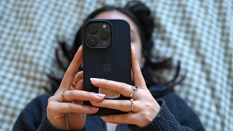 Eine junge Frau liegt mit dem Smartphone in der Hand auf dem Bett.