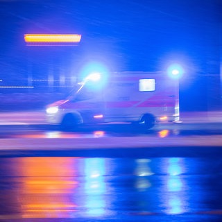 Ein Krankenwagen fährt im Dunkeln mit Blaulicht auf einer Straße. Bei Frankenthal ist ein Autofahrer nach einem Überholmanöver gestorben.