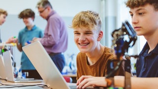 Zwei Schüler an einem Laptop und mit einem kleinen Roboter.