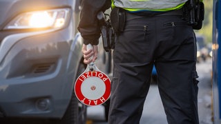 Ein Bundespolizist steht mit einer Kelle an einer Kontrollstelle auf der A64 bei Trier (Archivbild) - Das OVG Koblenz hat entschieden: Die Grenzkontrollen zwischen Deutschland und Luxemburg waren rechtswidrig.