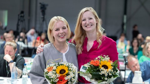 Christin Sauer und Carolin Cloos lachen mit Blumensträußen in die Kamera. Sie sind die neuen Landesvorsitzenden der Grünen Rheinland-Pfalz 