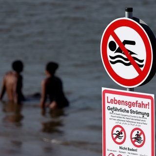 Ein Schild warnt vor gefährlicher Strömung und Lebensgefahr beim Baden im Rhein.