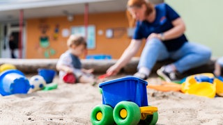 Ein Kind spielt mit einer Erzieherin im Sandkasten einer Kita.