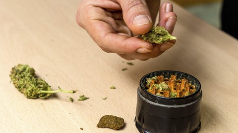 Hände einer Person, die Marihuana in einem Grinder zubereitet