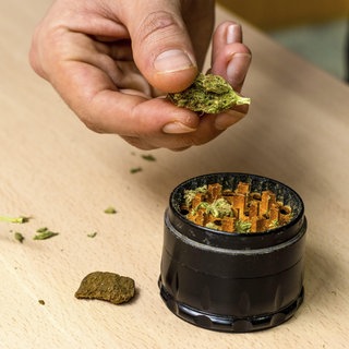 Hände einer Person, die Marihuana in einem Grinder zubereitet