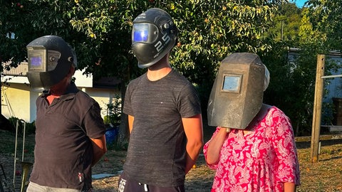 Zwei Männer und eine Frau haben einen Schweißhelm auf und beobachten die Sonnenfinsternis in Salem in Baden-Württemberg.