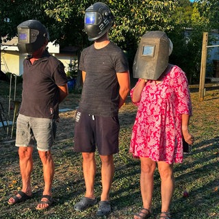 Zwei Männer und eine Frau haben einen Schweißhelm auf und beobachten die Sonnenfinsternis in Salem in Baden-Württemberg.