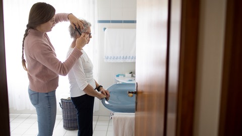 Junge Frau kämmt älterer Frau die Haare. Pflegereform belastet pflegende Angehörige 