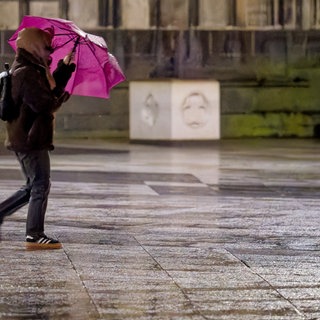 Eine Frau geht bei Regen und Wind mit einem Schirm durch eine Stadt (Archivbild)