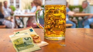 Bargeld liegt neben einem Bierglas auf einem Tisch vor einer Hütte: Auf den Pfälzerwaldhütten in RLP kann man meist nur mit Bargeld zahlen. Das wollen die Tourismusverbände im Land ändern.