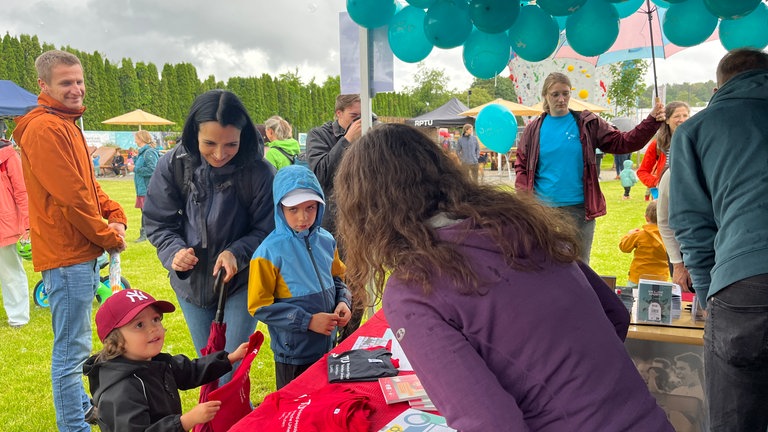 Ein Kind steht mit einem Shirt an einem Stand des Unisport: Der Unisport der Rheinland-Pfälzischen Technischen Universität Kaiserslautern-Landau (RPTU) hat auf dem Campus einen Abenteuerspielplatz eröffnet. Das Kitz-Land können Kinder mit einer Unisport-Karte besuchen.