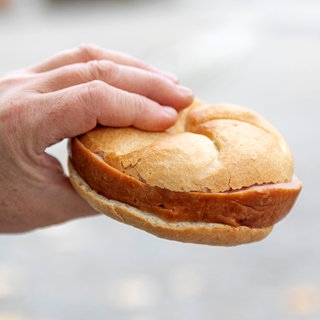 Eine Hand hält ein Brötchen mit Fleischkäse - Polizei ermittelt gegen Frau, die Fleischkäse-Brötchen in Kaiserslautern gestohlen haben soll