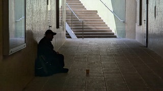Ein Mann sitzt in einer Unterführung und bettelt.
