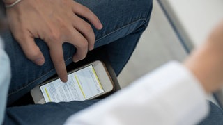 Wie mit KI bei Prüfungen umgehen? Das fragen sich Gymnasien in Kaiserslautern (Schüler scrollt mit Smartphone unter dem Tisch).