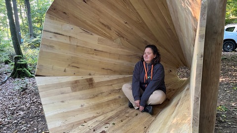 Den Wald mit allen Sinnen genießen: Verena Wasem, Tourismus-Mitarbeiterin der Verbandsgemeinde Nordpfälzer Land, im "Waldlauscher", einem großen Trichter aus Holz. 