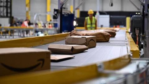 Pakete auf einem Förderband. Amazon erhält Baugenehmigung für Logistikzentrum in Zweibrücken.