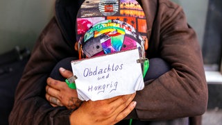 Bettler sitzt auf der Straße mit einem Schild, auf dem steht: obdachlos und hungrig. 