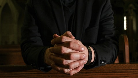 Das Symbolfoto zeigt einen Priester, er kniet in einer Kirche und hat die Hände fest zum Gebet gefaltet. In Koblenz beginnt das Berufungsverfahren gegen einen umstrittenen katholischen Priester aus dem Westerwald, dem Kindesmissbrauch vorgeworfen wird.