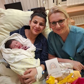 Neugeborenes Baby auf dem Arm der Mutter, daneben die Hebamme des Westpfalz-Klinikums in Kaiserslautern