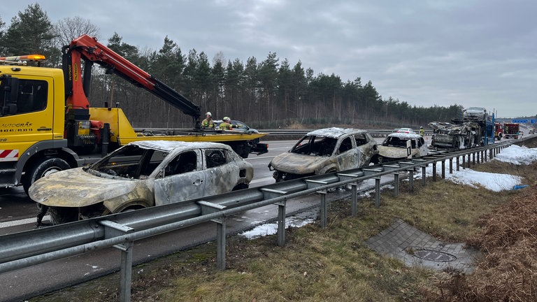 Ein Abschleppwagen mit Kran steht auf der A6 vor mehreren ausgebrannten Autos.