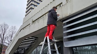 Ein Mann hängt am Rathaus Kaiserslautern eine Kamera auf