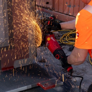 Ein Arbeiter schneidet ein Metallbauteil mit einem elektrischen Winkelschleifer während Bau- oder Montagearbeiten.