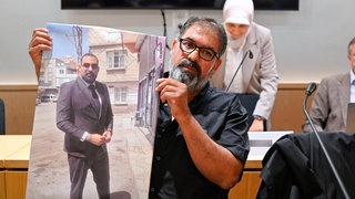 Erdal Calar, Vater des getöteten Zugbegleiters Serkan Calar, hält im Verhandlungssaal des Landgerichts ein Bild des Opfers in den Händen.