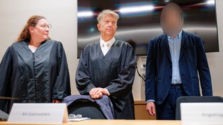 Der Angeklagte (rechts) steht im Verhandlungssaal neben seinen Rechtsanwälten
