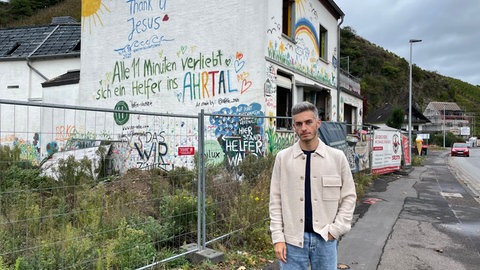 Mann steht vor einem bemalten, aber zerstörten Haus im Ahrtal für die 360-Grad-Reportage.
