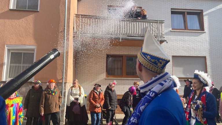 Menschen auf einem Balkon im ersten Stock werden mit einer Konfettikanone beschossen: Auch "Zaungäste" kommen am Schwerdonnerstag am Karneval nicht vorbei - so wie hier in Mülheim-Kärlich. 