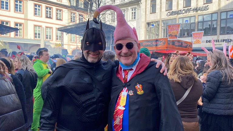 Zwei Männer in Kostümen stehen in der Koblenzer Alstadt. An Schwerdonnerstag in Koblenz ist auch Batman unterwegs. Mit dabei hat er seinen treuen Freund Flamingo.