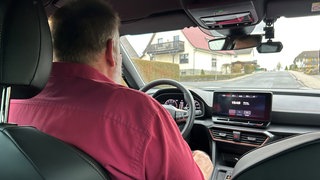 Detektiv sitzt im Auto und beobachtet Umfeld, Ansicht von der Seite.