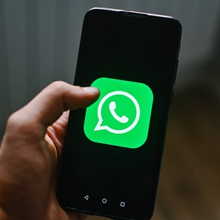 Eine männliche Hand hält ein Handy mit dem grünen Logo von WhatsApp auf dem Display