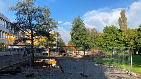 Neben einem Gebäude steht ein Bagger, hinter einem Bauzaun wurde ein Loch ausgehoben. An vier Schulen in Remagen werden die Schulhöfe und Gebäude umgestaltet und an den Klimawandel angepasst.
