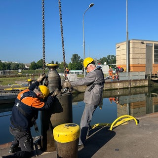 Zwei Männer arbeiten an einer Schleuse und ziehen an einem großen Metallteil.