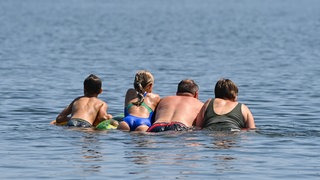 Eine Familie schwimmt auf einer Luftmatratze in einem Badesee - der Westerwaldkreis warnt vor Badedermatitis.