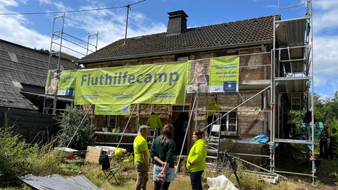 An einem alten Fachwerkhaus in Insul ist ein Gerüst angebracht. An dem Gerüst ist ein großes, gelbes Transparent angebracht. Daraus steht: Fluthilfecamp.