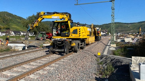 Ein gelber Bagger arbeitet an der Ahrtalbahn in Dernau: Bald soll die Züge wieder durchgängig zwischen Remagen und Ahrbrück fahren können. 