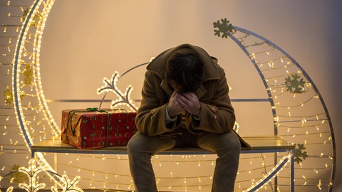 Ein Mann sitzt allein mit gesenktem Kopf vor festlicher Weihnachtsbeleuchtung