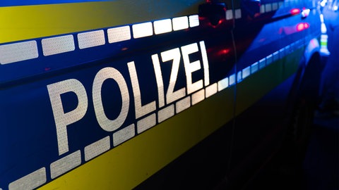Ein Streifenwagen, Einsatzwagen der Polizei, steht mit Schriftzug bei Dunkelheit an einem Unfallort. (Sujetbild)
