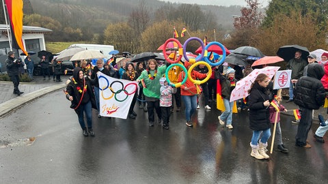 Menschen in Brachbach halten die Olympischen Ringe und Transparente zur Begrüßung von Jacqueline Pfeifer hoch.