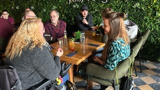 Menschen sitzen an einem Tisch im Restaurant mit dem Angebot "Stille Stunde" und unterhalten sich.