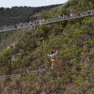 Ein mann geht auf einer Slackline dirket neben der Geierlay Hängeseilbrücke.