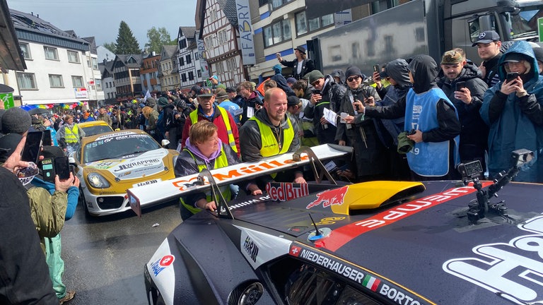 Ordner vom Motor-Sport-Club Adenau schieben einen Rennwagen beim "Racing Day" durch die Innenstadt.